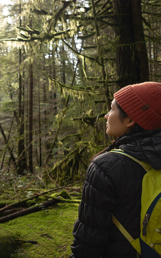 woman hiker pausing to meditate while forest bathing in a winter forest. North Vancouver, British Columbia, Canada.